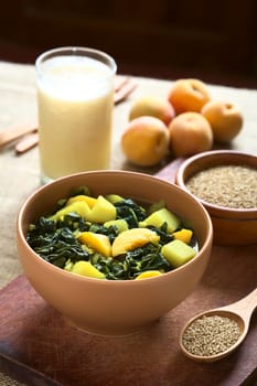 Bowl of spinach, peach and potato curry dish with sesame seeds, peaches and lassi in the back photographed with natural light (Selective Focus, Focus one third into the curry dish)