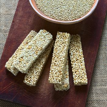 Overhead shots of quinoa cereal bars, one with honey the other mixed with amaranth, with bowl of raw white quinoa on wooden board photographed with natural light (Selective Focus, Focus on the upper cereal bars)