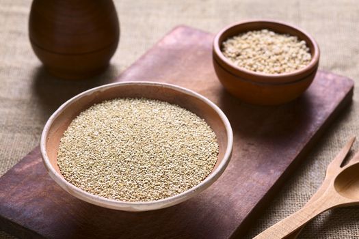 Raw white quinoa (lat. Chenopodium quinoa) grain seeds in bowl with popped quinoa cereal in the back on wooden board photographed with natural light (Selective Focus, Focus one third into the raw quinoa seeds)