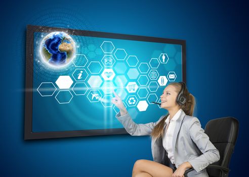Businesswoman in headset pressing touch screen button on virtual interface with Globe and honeycomb shaped icons, on blue background. Element of this image furnished by NASA