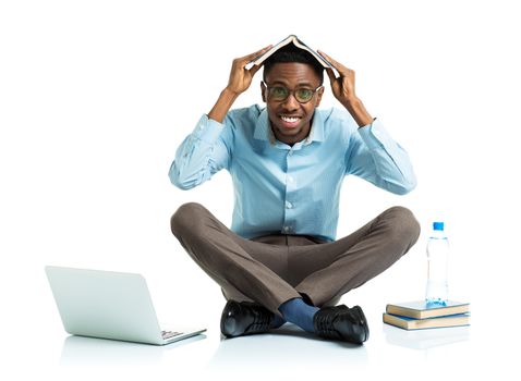 Happy african american college student sitting on white background with laptop and some books