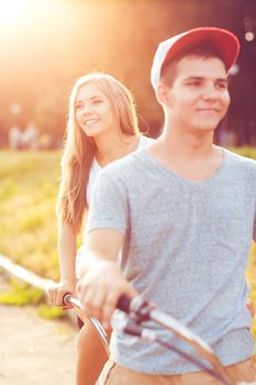 Happy couple - young man and woman riding a bicycle in the park outdoors