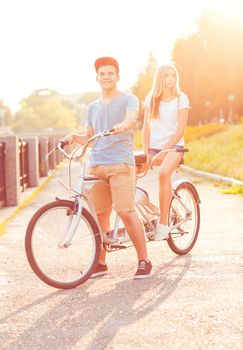 Happy couple - young man and woman riding a bicycle in the park outdoors