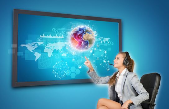 Businesswoman in headset using touch screen interface with Globe, network of person icons and other elements, on blue background. Element of this image furnished by NASA