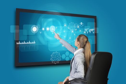 Businesswoman using touch screen interface with network of person icons, graph and other elements, on blue background