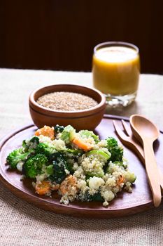 Cooked white quinoa seeds with fried vegetables (carrot, broccoli, spinach, zucchini, corn) on wooden plate, sesame seeds and mango juice in the back, photographed with natural light (Selective Focus, Focus on the front of the dish)