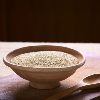 Raw white quinoa (lat. Chenopodium quinoa) grain seeds in bowl on wooden board photographed with natural light (Selective Focus, Focus one third into the raw quinoa seeds)