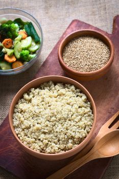 Overhead shot of cooked white quinoa seeds in bowl with sesame and fried vegetables in the back photographed with natural light (Selective Focus, Focus on the quinoa)