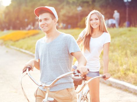 Happy couple - young man and woman riding a bicycle in the park outdoors