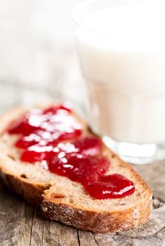 Bread with strawberry jam and glass of milk on wooden table