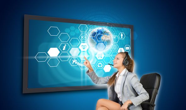 Businesswoman in headset pressing touch screen button on virtual interface with honeycomb shaped icons and Globe with radiant figures, on blue background. Element of this image furnished by NASA