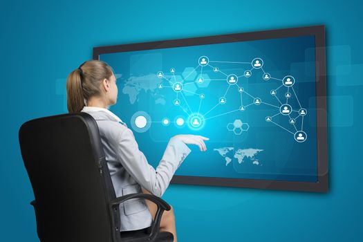 Businesswoman using touch screen interface with network of person icons and other elements, on blue background