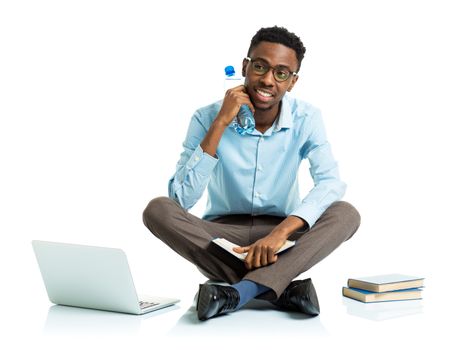 Happy african american college student sitting on white background with laptop and some books