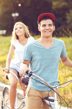 Happy couple - young man and woman riding a bicycle in the park outdoors