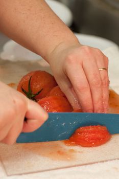 Fresh tomatoes being diced on a cutting board by a female chef with a ceramic knife.