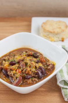 Fresh homemade chili in a white bowl with a homemade cheddar and garlic biscuit on side.