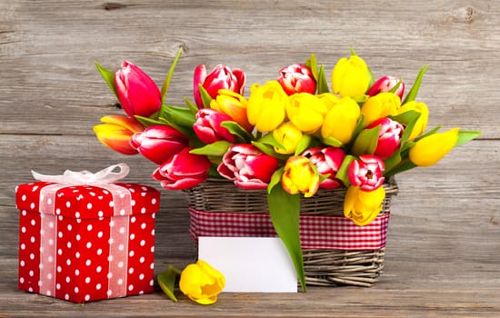 spring tulips in wooden basket, red polka-dot gift box. happy mothers day, romantic still life, fresh flowers. on wooden background