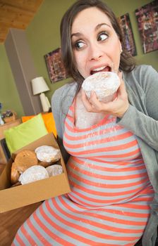 Happy pregnant woman making a mess eating donuts