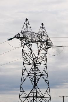 Two Guys Cleaning Big Electrical Pylon with a Cloudy Sky