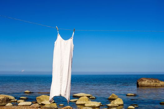 White dress hanging on a rope on the sea background