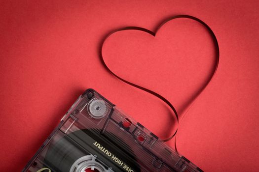 Audio cassette tape on red backgound. Film shaping heart, Valentine postcard. Label text love songs.