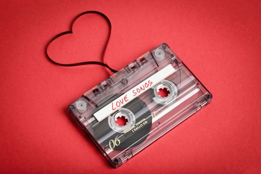 Audio cassette tape on red backgound. Film shaping heart, Valentine postcard. Label text love songs.