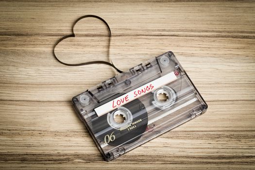 Audio cassette tape on wooden backgound. Film shaping heart, Valentine postcard. Label text love songs.