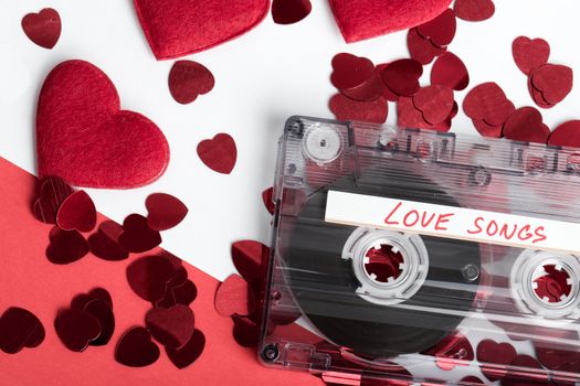 Audio cassette tape on red backgound with fabric heart, Valentine postcard. Love concept with evelope and confetti