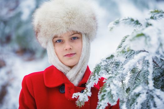 Happy teenager girl in fur hat walking in winter park