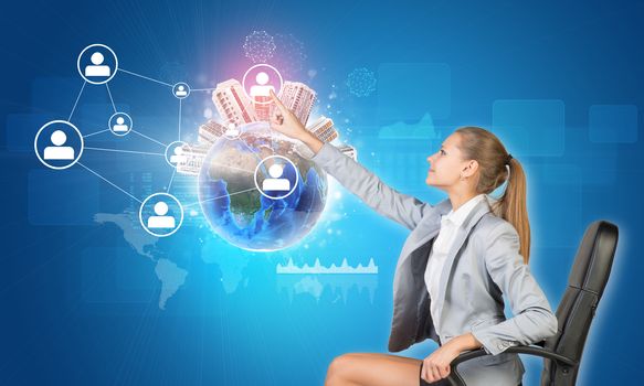 Businesswoman pressing touch screen button on virtual interface featuring Globe with buildings on top and network with person icons, on blue background. Element of this image furnished by NASA