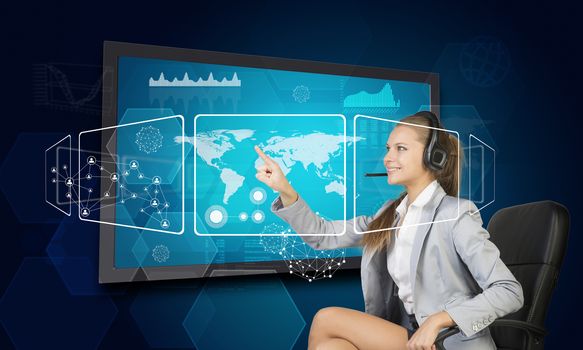 Businesswoman in headset using touch screen interface with world map, graphs and other elements, on blue background