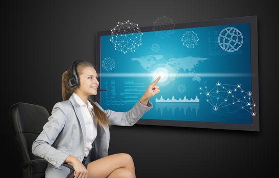 Businesswoman in headset using touch screen interface with world map, graphs and other elements, on dark background