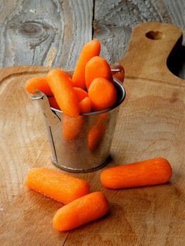 Heap of Fresh Raw Peeled Baby Carrots in Tin Bucket closeup on Wooden Cutting Board