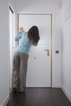brown trousers green jersey woman back looking to peephole interior house hall white door wooden floor