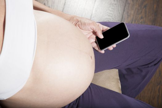 pregnant woman purple trousers bare belly sit showing in her hand blank screen smartphone