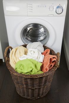 brown wooden wicker basket full of dirty clothes sheets and towels at door of white washing machine