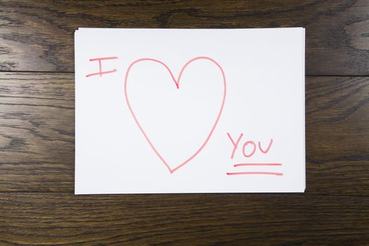 I love you text written with orange marker on white paper over brown wooden background