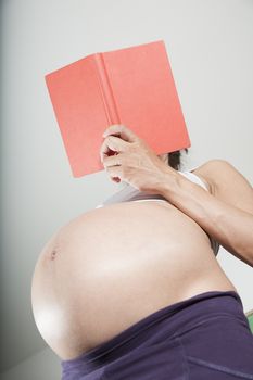 pregnant woman purple trousers bare belly stand reading a red book