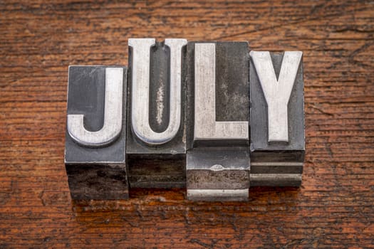 July word in mixed vintage metal type printing blocks over grunge wood