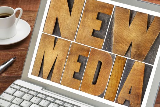 new media  -  words in letterpress wood type on a laptop screen with a cup of coffee