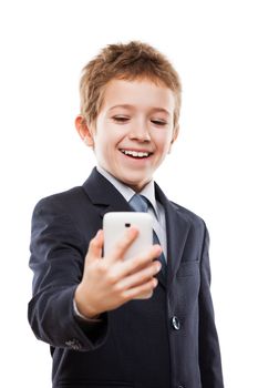 Little smiling child boy in business suit hand holding mobile phone or smartphone making selfie portrait photo white isolated