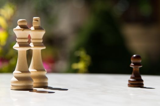 Chess pieces, pawn and queens on white table with blurry background.