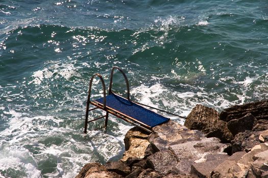 Pier on wavy sea and beach with stones.