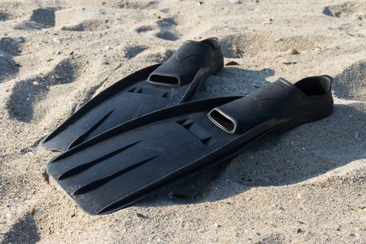 Black plastic flippers on sea sand.