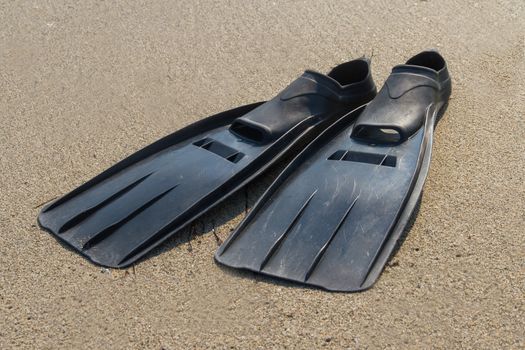 Black plastic flippers on sea sand.