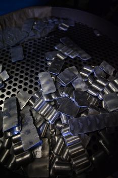 A group of loose and attached, manganese briquettes strewn over a metal grid with a blue light, highlighting the edges.