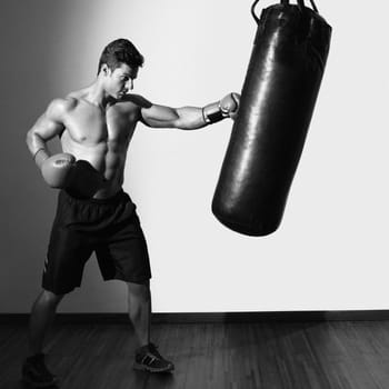 Full length of a shirtless muscular boxer with punching bag in gym