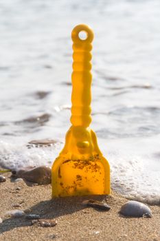 Yellow toy scoop standing on sand near sea with foam.
