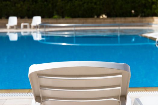 Sunbed near blue clear swimming pool.
