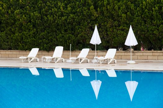 Sunbeds and umbrellas near blue clear swimming pool.